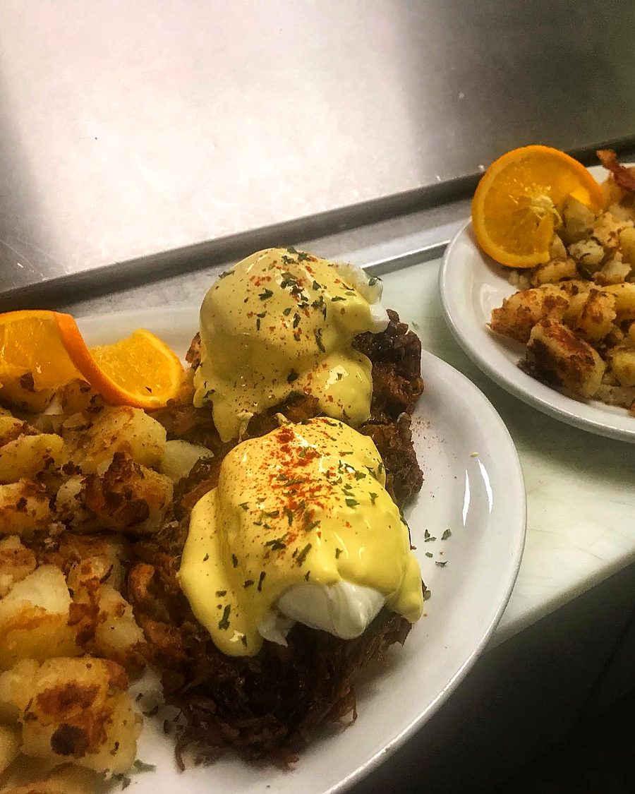 BBQ Pulled Pork Benny: poached eggs in hollandaise over slow-cooked pulled pork, with crispy hash browns and an orange slice