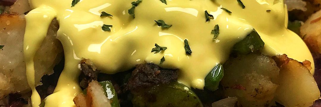 Corned beef hash: diced hash browns with smoked meat, green peppers and onions under poached eggs and hollandaise sauce, sprinkled with parsley