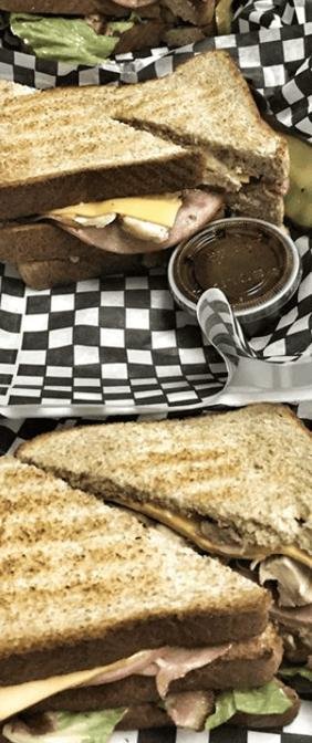 Two toasted sandwiches with ham, cheese and lettuce on black-and-white checkered paper